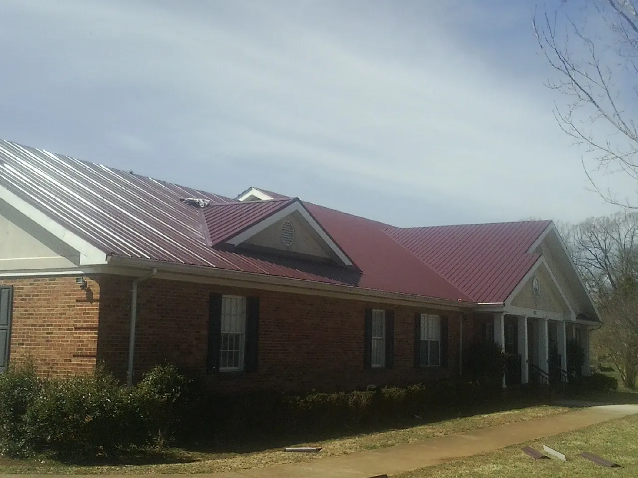 Red metal roof with gabled entries on a long brick building, from a Hail Damage Roof Repair job in Biddeford Pool