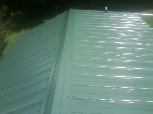 New green metal panels meeting at the ridge of a roof — Flat Roof Repair work by our crew in Biddeford Pool