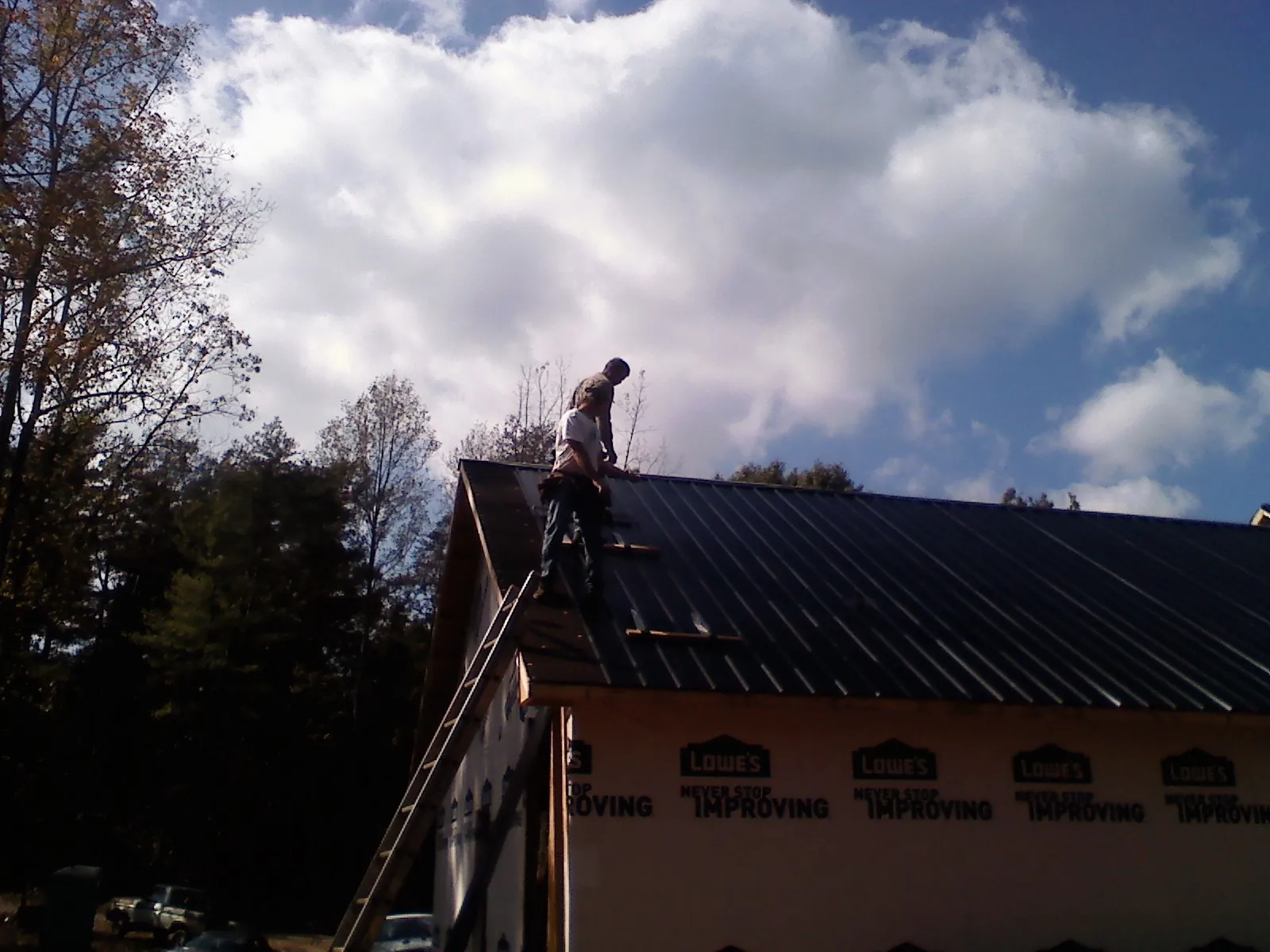 Roofer fastening dark metal panels high against a cloudy sky, from a Roof Inspection job in Biddeford Pool