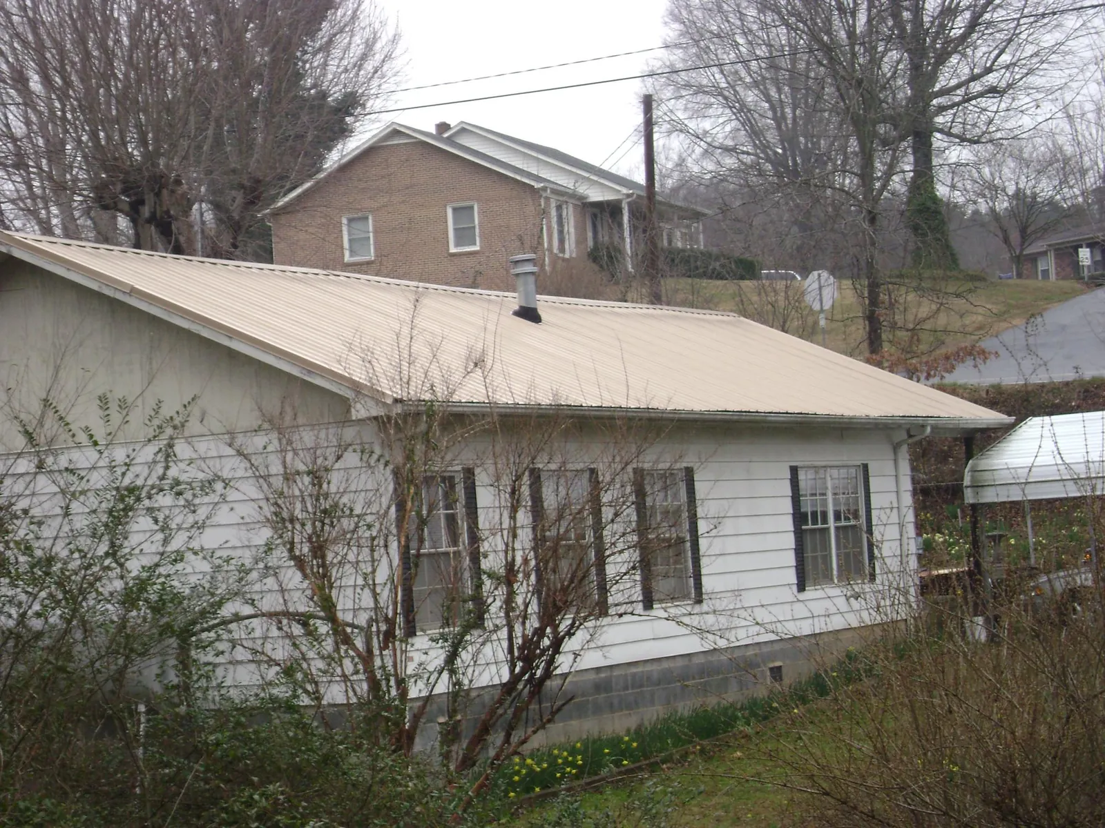 Tan metal roof on a white sided house set into a hillside — Commercial Roofing by Roofing Brothers in Biddeford Pool